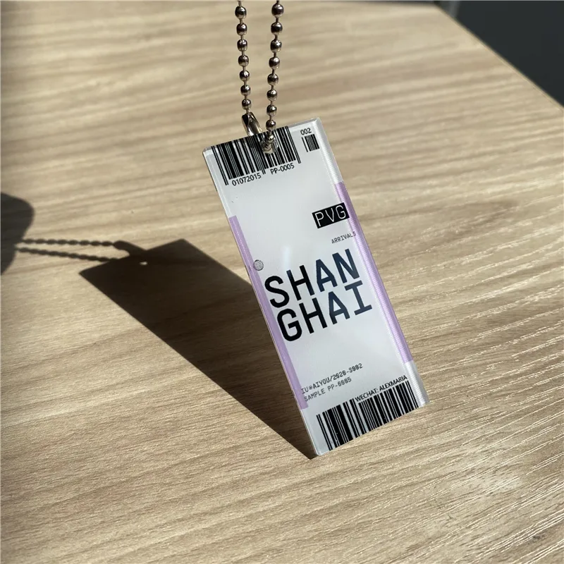 Boarding-pass shaped clear acrylic keychain hanging against daylight