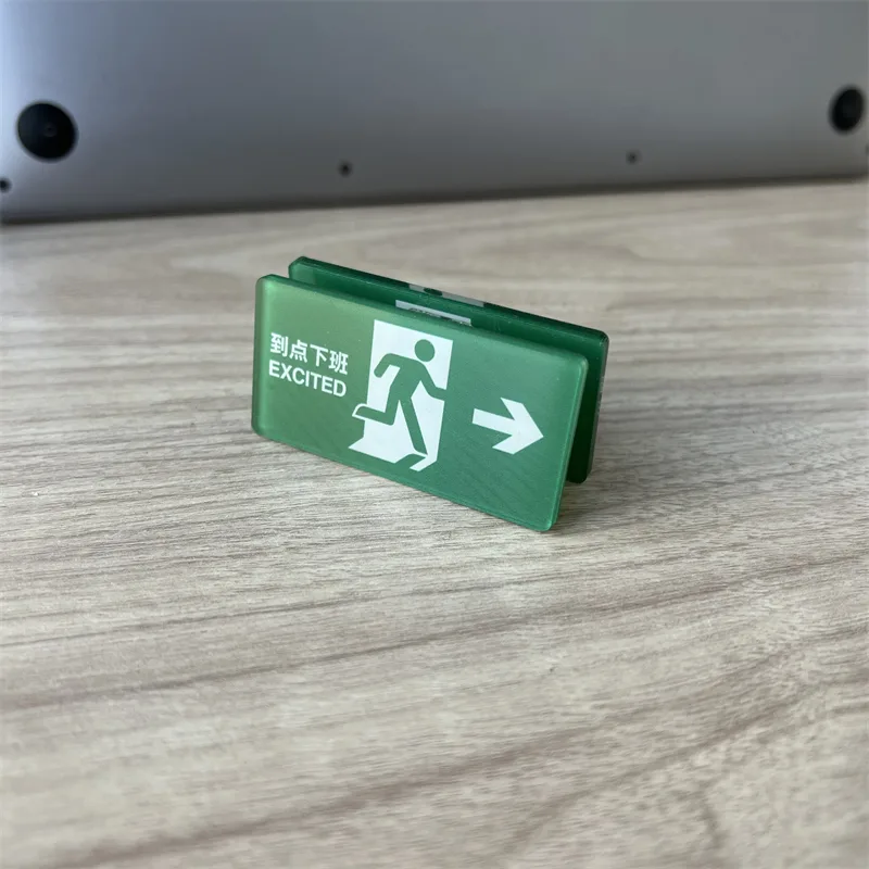 Green exit-sign shaped acrylic keychain standing on a wooden desk