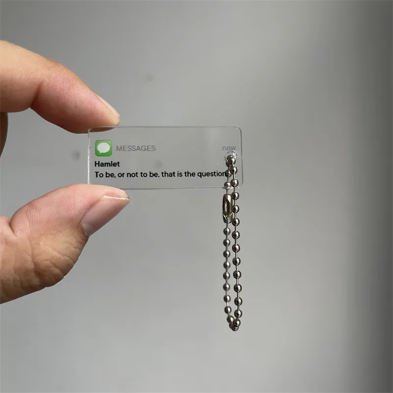 Fingers holding a small clear acrylic keychain with printed Hamlet quote artwork
