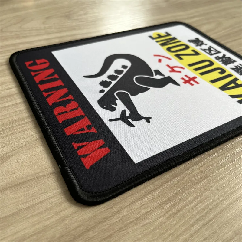 Woven mouse pad with stitched edge and a printed Kaiju Zone Godzilla design, lying on a wooden desk