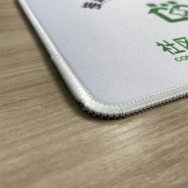 Close-up of a stitched edge on a pale printed mouse pad, showing the overlock stitching around the corner