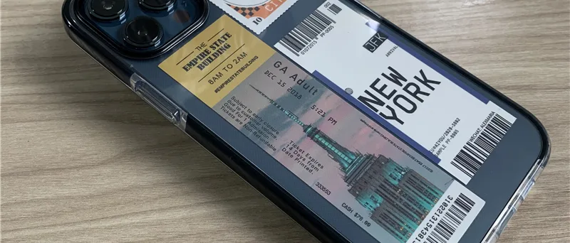 Clear phone case printed with a New York ticket-collage design, photographed on a wooden desk